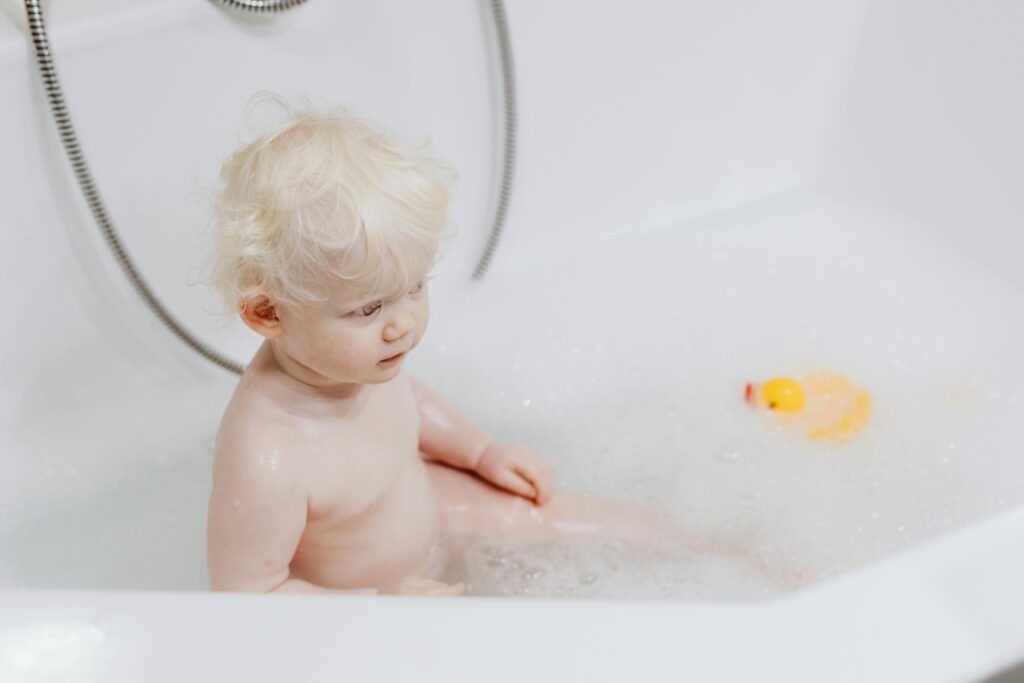 Photograph of a Child with Blond Hair Sitting in a Bathtub with Bubbles